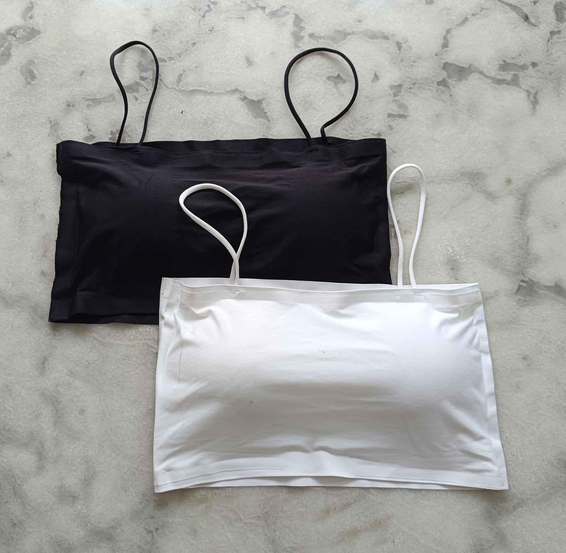 Black and white comfortable lingerie pack with thin straps laid flat on marble surface